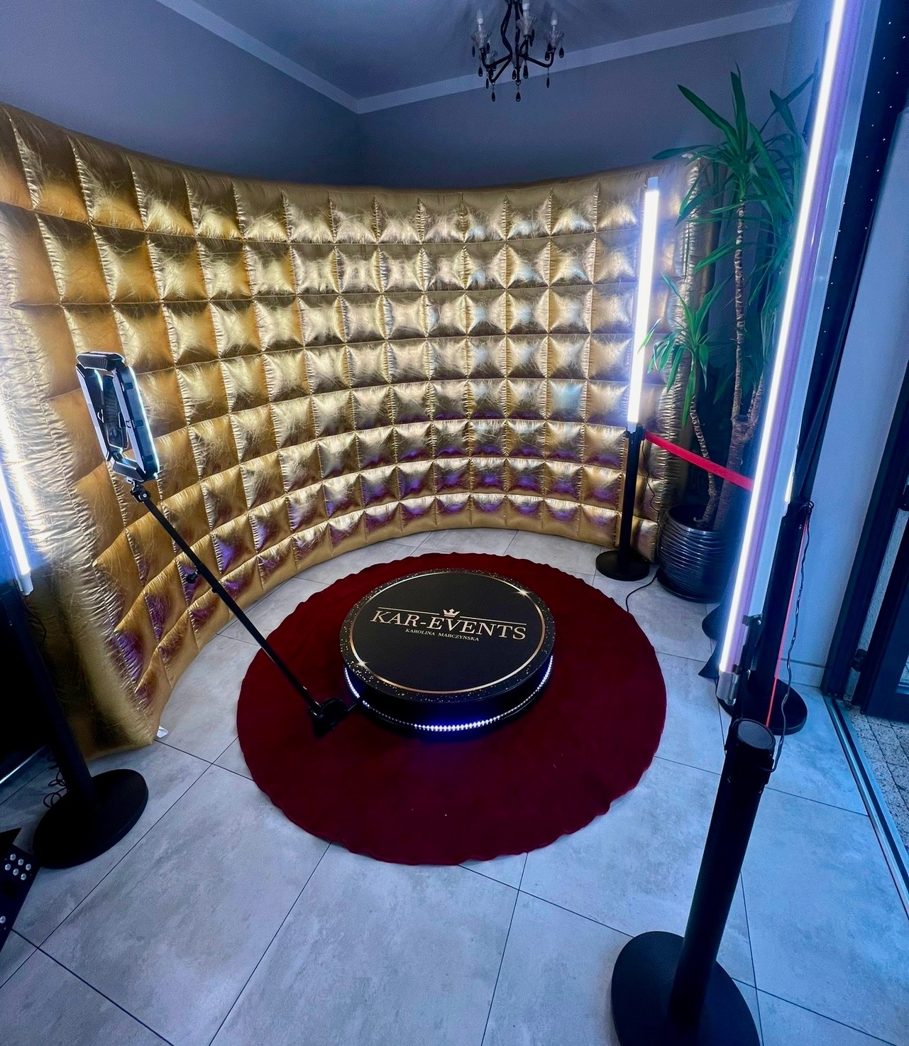 Złota, dmuchana ścianka fotobudki z okrągłą platformą obrotową na czerwonym dywanie, oświetlona lampami LED, z widocznym logotypem 'KAR-EVENTS'.