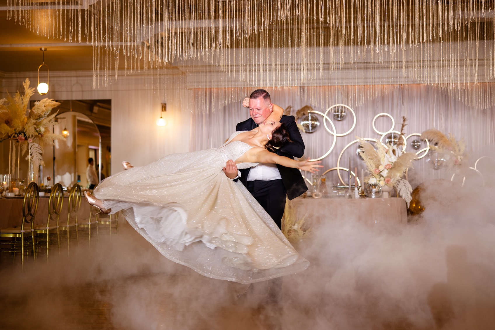 Para młoda podczas pierwszego tańca w chmurach dymu, sala udekorowana kwiatami i lustrzanymi kulami.