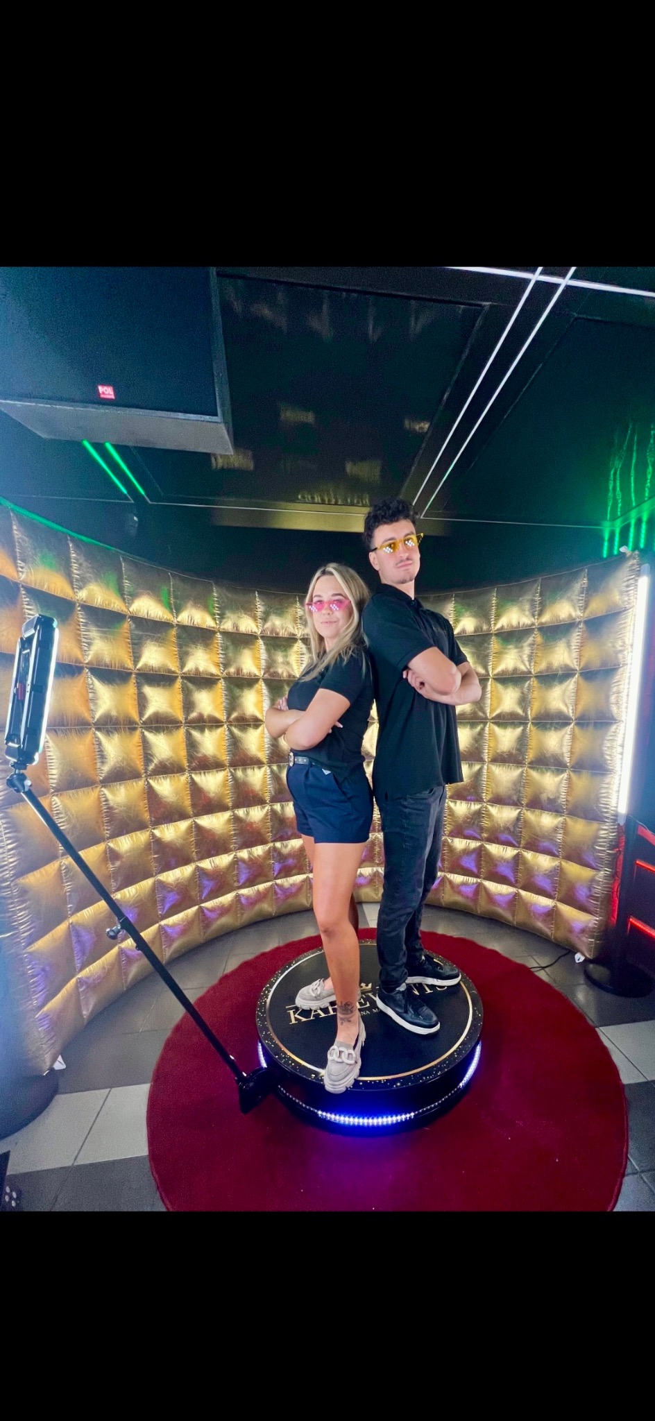 Para w okularach pozuje na obrotowej platformie fotobudki 360 w Szamocinie. Złote tło i oświetlenie LED.