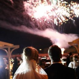 Sultex Beata Sulis - Para młoda obserwuje pokaz fajerwerków podczas nocnego wesela, widoczne jasne eksplozje na ciemnym niebie i sylwetki gości w tle.