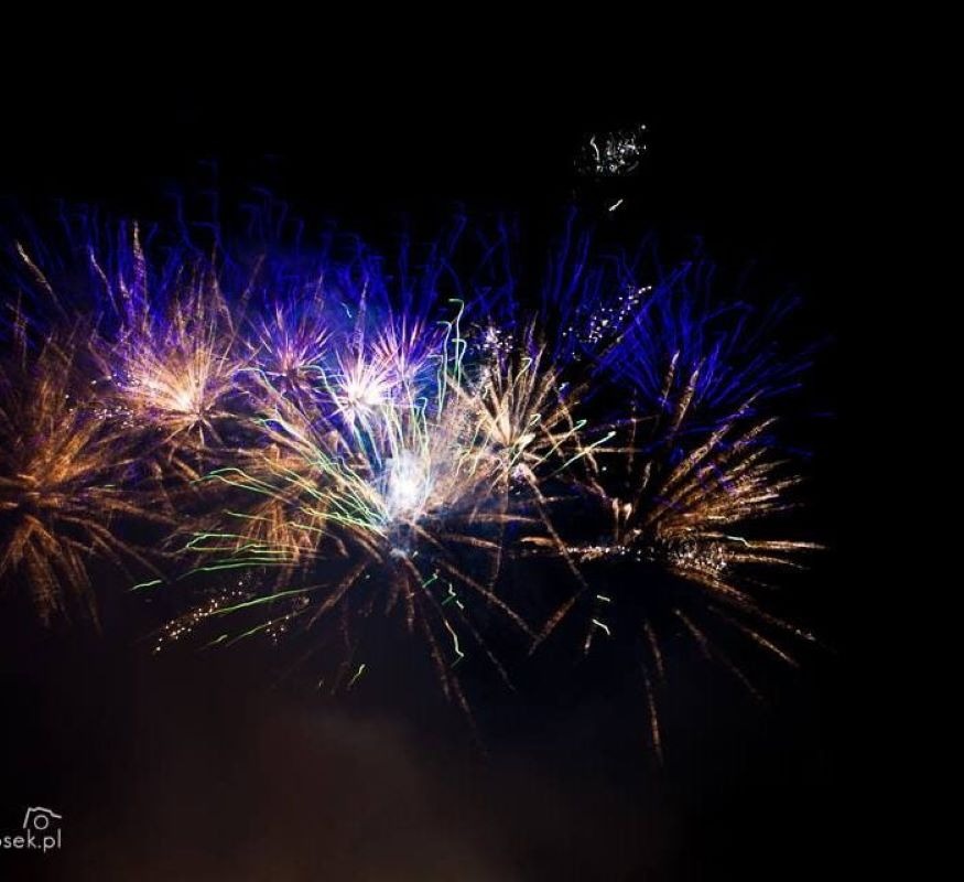 Wybuchające na nocnym niebie niebiesko-złote fajerwerki z zielonymi smugami, uchwycone w kadrze z lekkim efektem rozmycia ruchu.