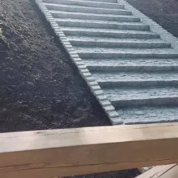 Kamienne schody prowadzące w górę wzgórza, z widoczną konstrukcją drewnianą w dolnej części kadru i drzewami w tle.