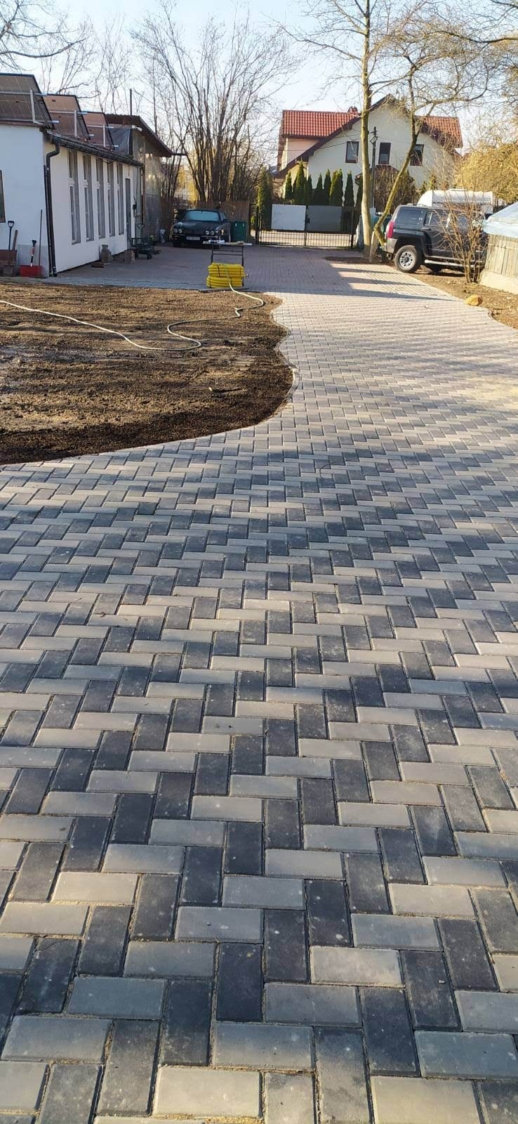 Ułożona kostka brukowa w jodełkę w Ożarowie Mazowieckim, obok świeżo nawieziona ziemia przygotowana pod trawnik, w tle zabudowa jednorodzinna.