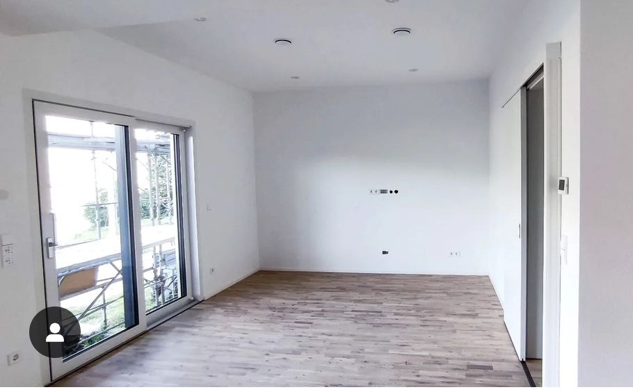 Wnętrze pokoju z jasnymi ścianami i ułożonym parkietem, widoczne okno przesuwne z rusztowaniem na zewnątrz i przesuwne drzwi wewnętrzne.