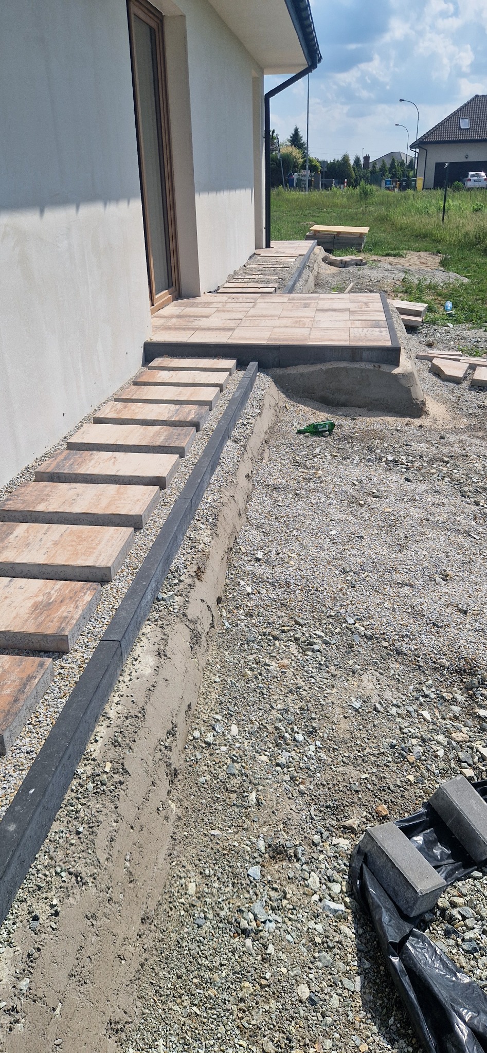 Wykonanie ścieżki z płyt betonowych prowadzącej do domu, obrzeża z szarego betonu, podłoże z kruszywa, widoczne przygotowania do dalszych prac.
