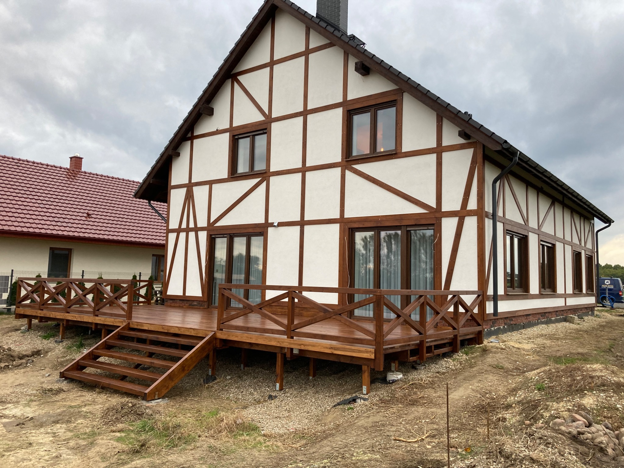 Nowoczesny dom z drewnianą konstrukcją szkieletową i przestronnym tarasem z brązowego drewna, widok z zewnątrz w pochmurny dzień.