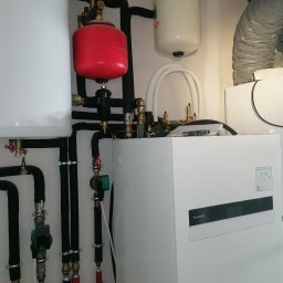 AEJ ENERGY Adam Jasina - Zmontowana instalacja pompy ciepła Panasonic Aquarea w Bolestraszycach. Widoczne rury, zbiorniki wyrównawcze i jednostka wewnętrzna. Estetyczny montaż.