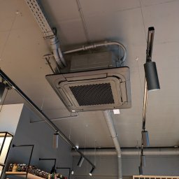 AEJ ENERGY Adam Jasina - Sufitowa klimatyzacja kasetonowa w szarej tonacji, widoczne rury instalacyjne i oświetlenie punktowe. Nowoczesny system klimatyzacji w lokalu komercyjnym.