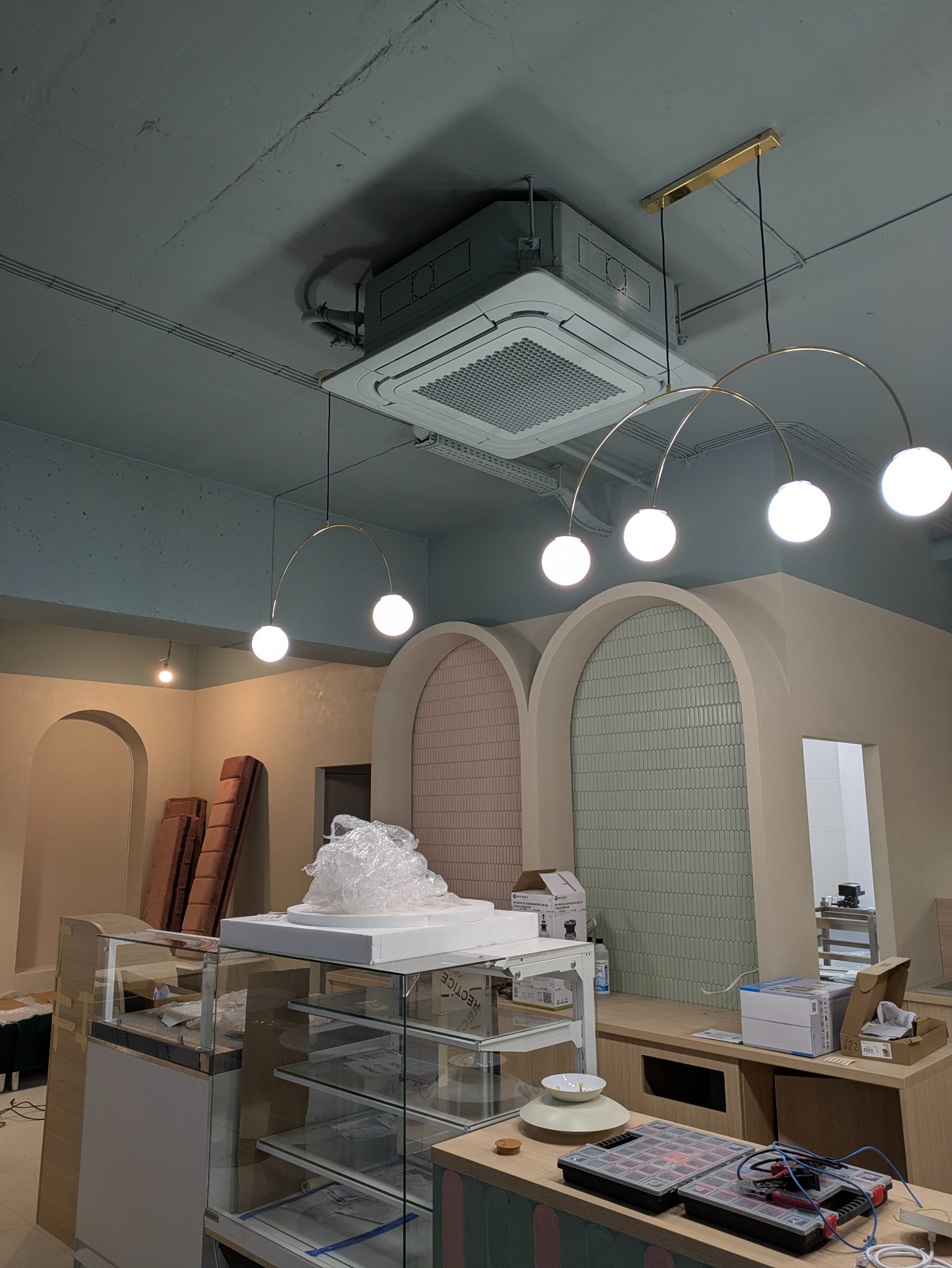 Kasetonowa klimatyzacja sufitowa w lokalu usługowym, widoczne elementy instalacji i oświetlenia. Lokal w trakcie wykańczania, widoczne materiały i narzędzia.