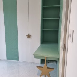 PPHU Prostyle Marcin Jankowski - Biało-zielona szafa z biurkiem w pokoju dziecięcym. Drzwiczki szafy zdobią złote gwiazdki, a biurko wspiera konstrukcja w kształcie gwiazdy.