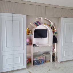 PPHU Prostyle Marcin Jankowski - Biała szafa wnękowa z półkami w kształcie łuku, podświetlona LED, z zabawkami i telewizorem, na marmurowej podłodze. Klasyczne frezowane fronty.