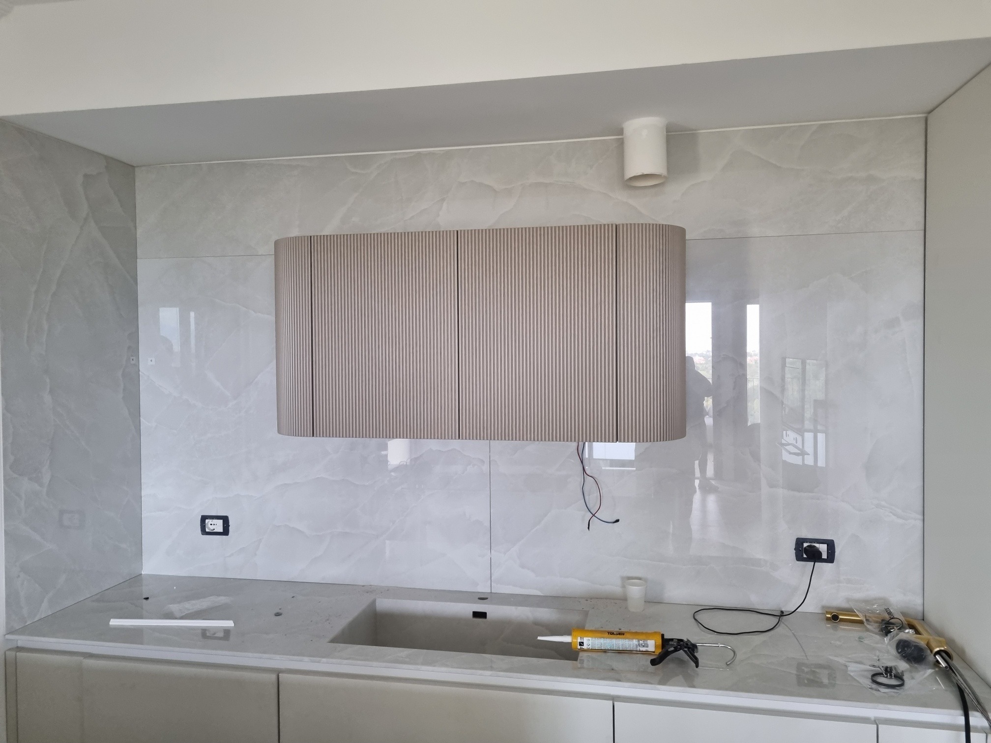 Montaż okapu i wykończenie ściany marmurową płytą w kuchni na wymiar w Gdańsku. Widoczne narzędzia i materiały montażowe.