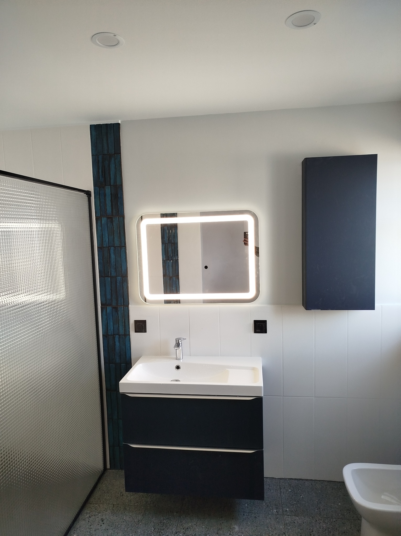 Nowoczesna łazienka po remoncie w Wałczu: umywalka z szafką w kolorze granatowym, podświetlane lustro, kabina prysznicowa ze szkła ornamentowego, płytki w odcieniach bieli i granatu.