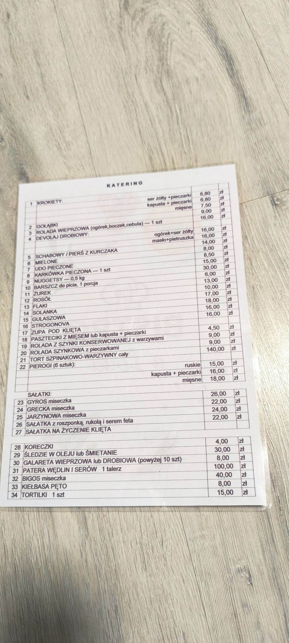 Menu cateringowe z cenami, zawierające listę dań takich jak krokiety, gołąbki, rolady, zupy, sałatki i pierogi.