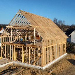 FachBud Rafał Szkwerko - Konstrukcja domu w technologii szkieletowej w trakcie budowy, widok z lotu ptaka, drewniane elementy konstrukcyjne na fundamencie, w tle zabudowa jednorodzinna.