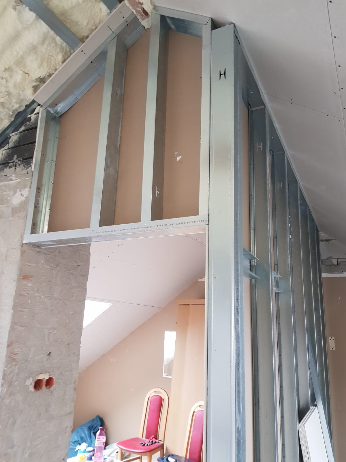 Stelaż z profili stalowych do montażu płyty kartonowo-gipsowej w pokoju na poddaszu, widoczne ocieplenie wełną mineralną i fragment ściany z instalacją elektryczną.