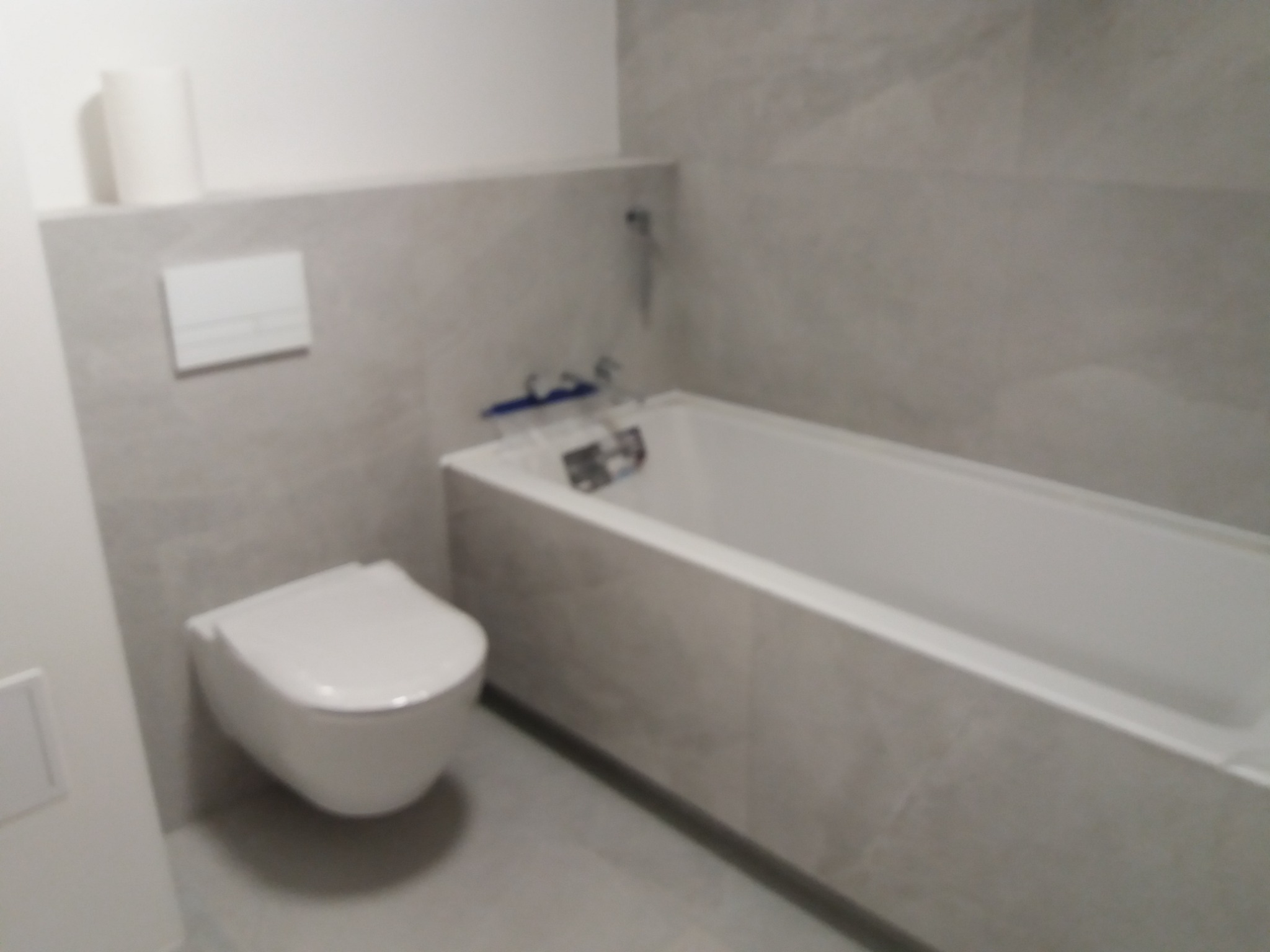 Nowoczesna łazienka wykończona w szarych płytkach imitujących kamień, z podwieszaną toaletą i zabudowaną wanną.