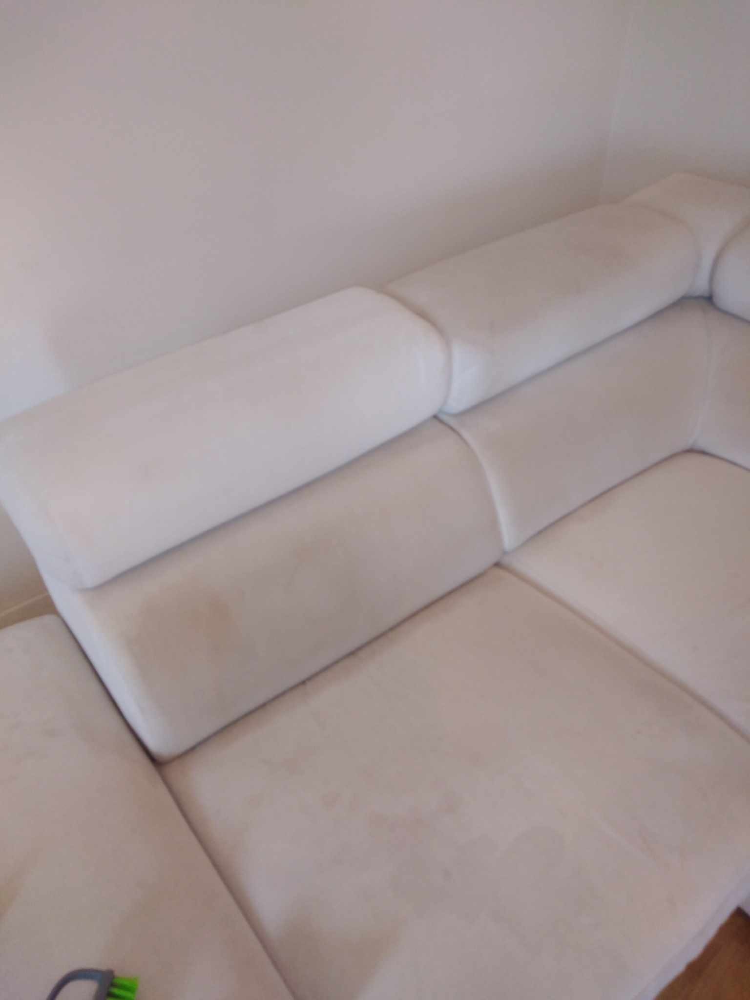 Fragment narożnika z jasną tapicerką, widoczne plamy przed czyszczeniem, w rogu kadru fragment szczotki.