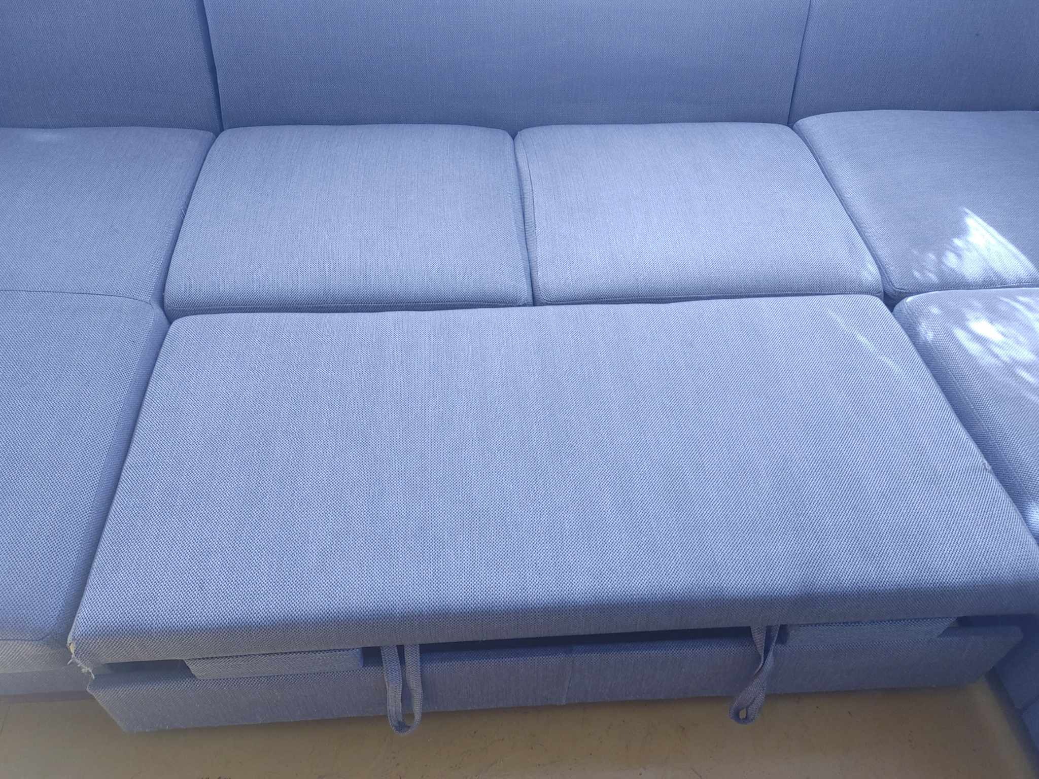 Jasnoszara, modułowa sofa z wysuwanym siedziskiem i teksturowaną tapicerką.