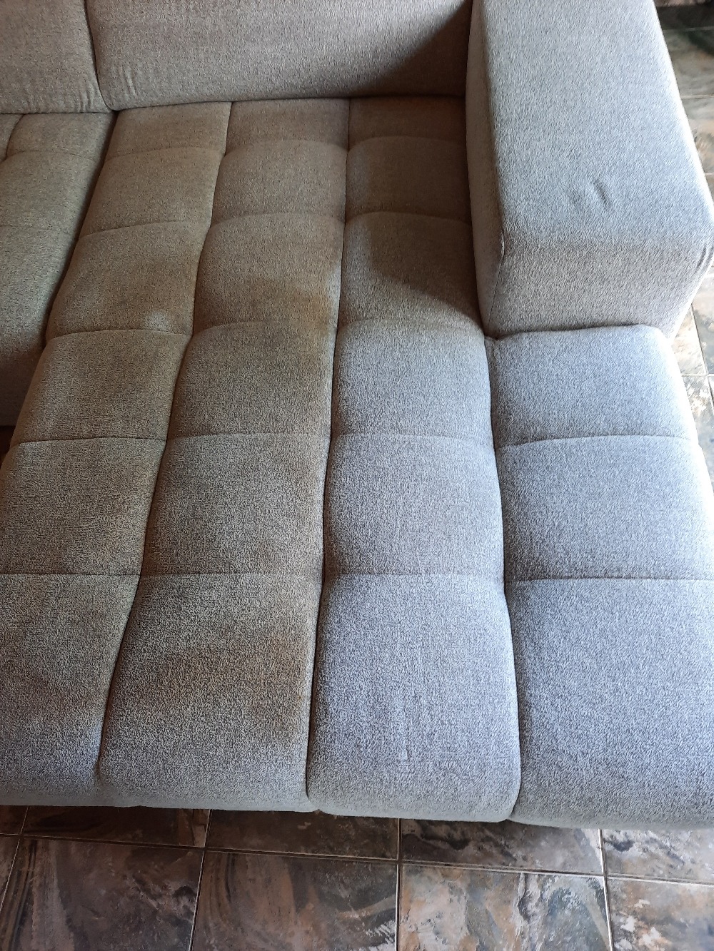 Fragment sofy modułowej z wyraźną różnicą w czystości tapicerki: po lewej stronie widoczne zabrudzenia, po prawej - świeżo wyczyszczona powierzchnia.