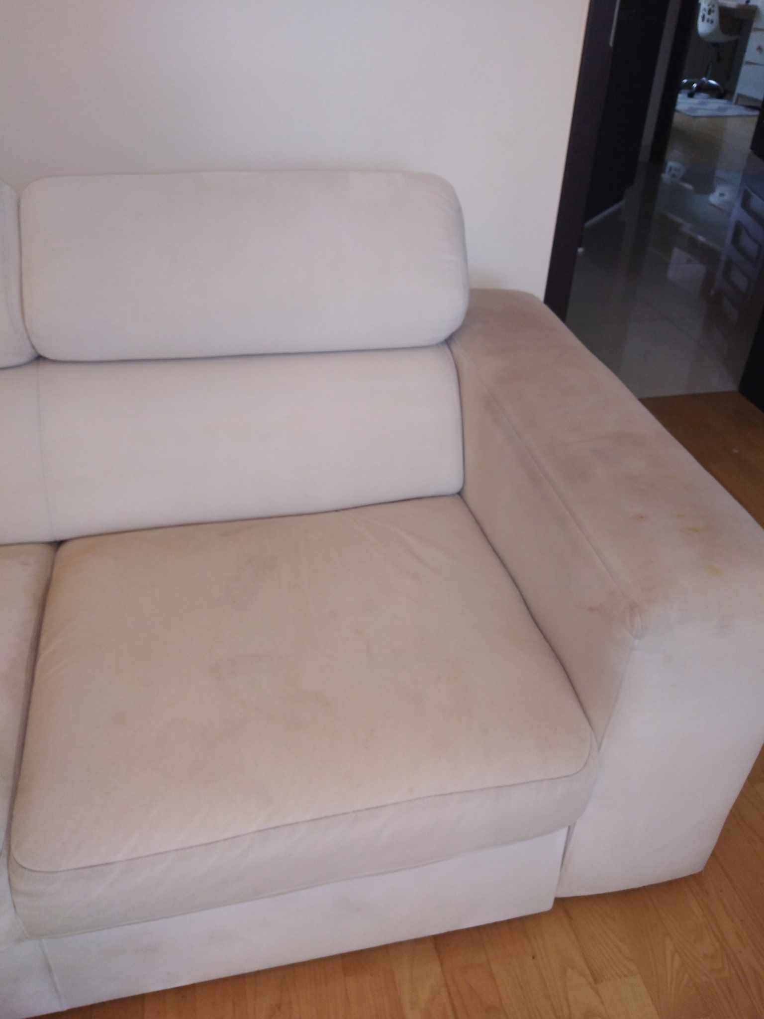 Fragment jasnej, tapicerowanej kanapy z widocznymi plamami na siedzisku i podłokietniku, na drewnianej podłodze.