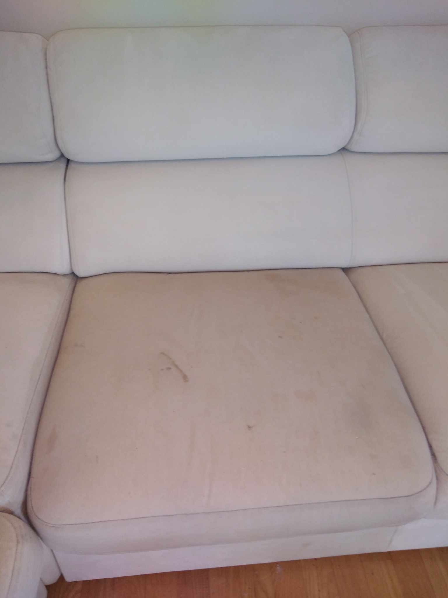 Brudna, jasna kanapa z widocznymi plamami na siedzisku, wymagająca prania.