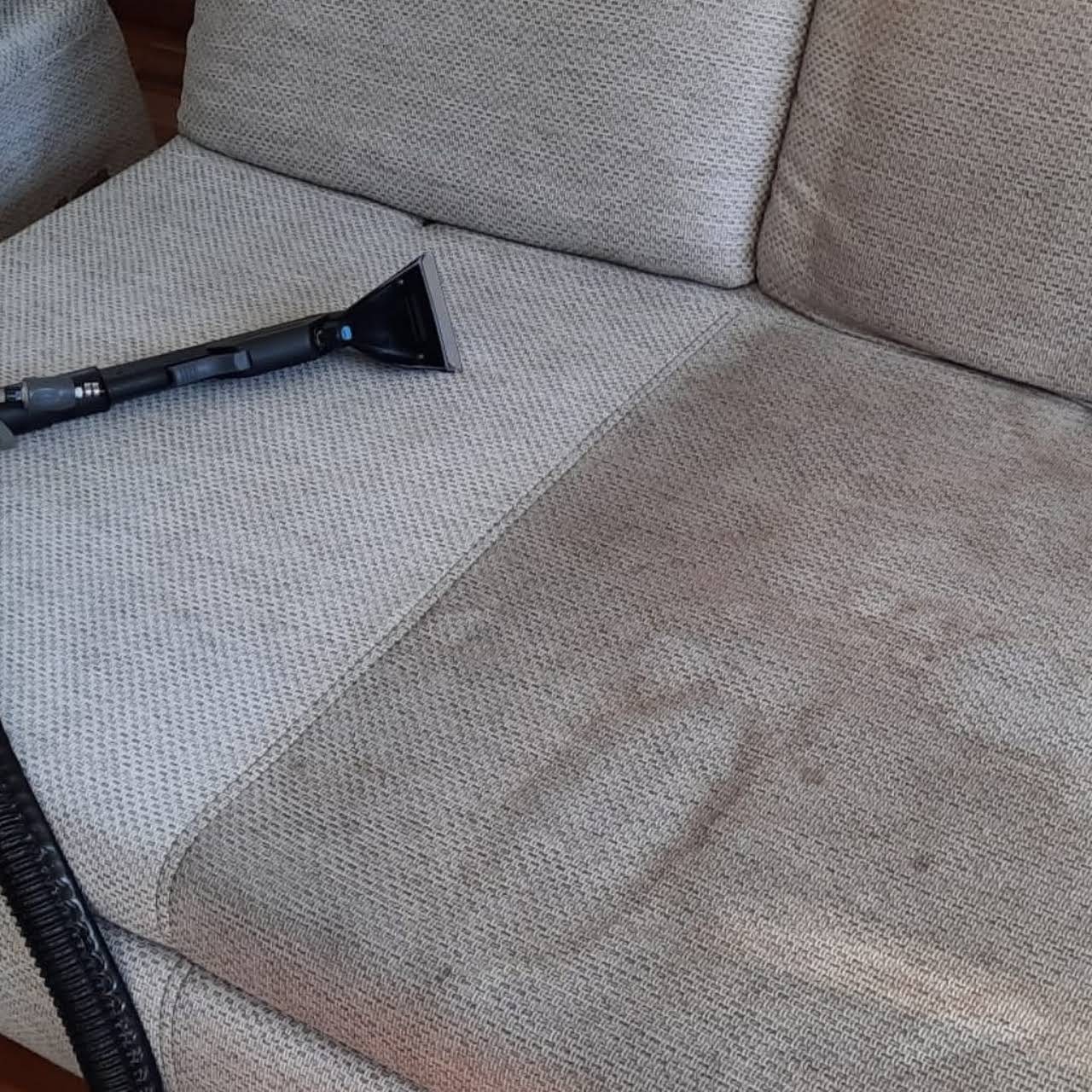 Czyszczenie tapicerki kanapy szarym odkurzaczem piorącym, widoczna różnica w czystości między obszarem wyczyszczonym a zabrudzonym.