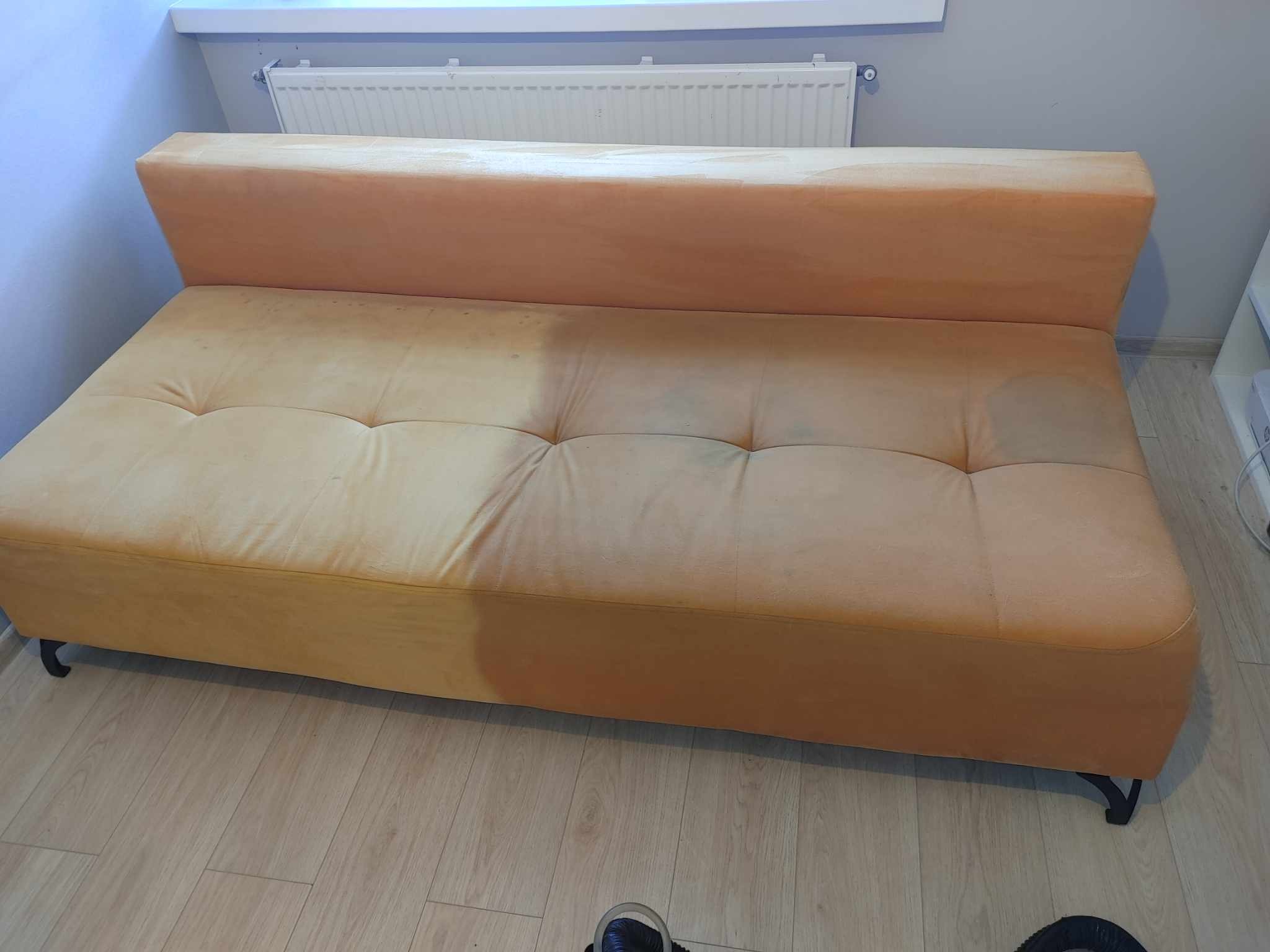 Żółta kanapa z wyraźną różnicą w czystości: lewa strona z widocznymi plamami, prawa po czyszczeniu, na podłodze panele.