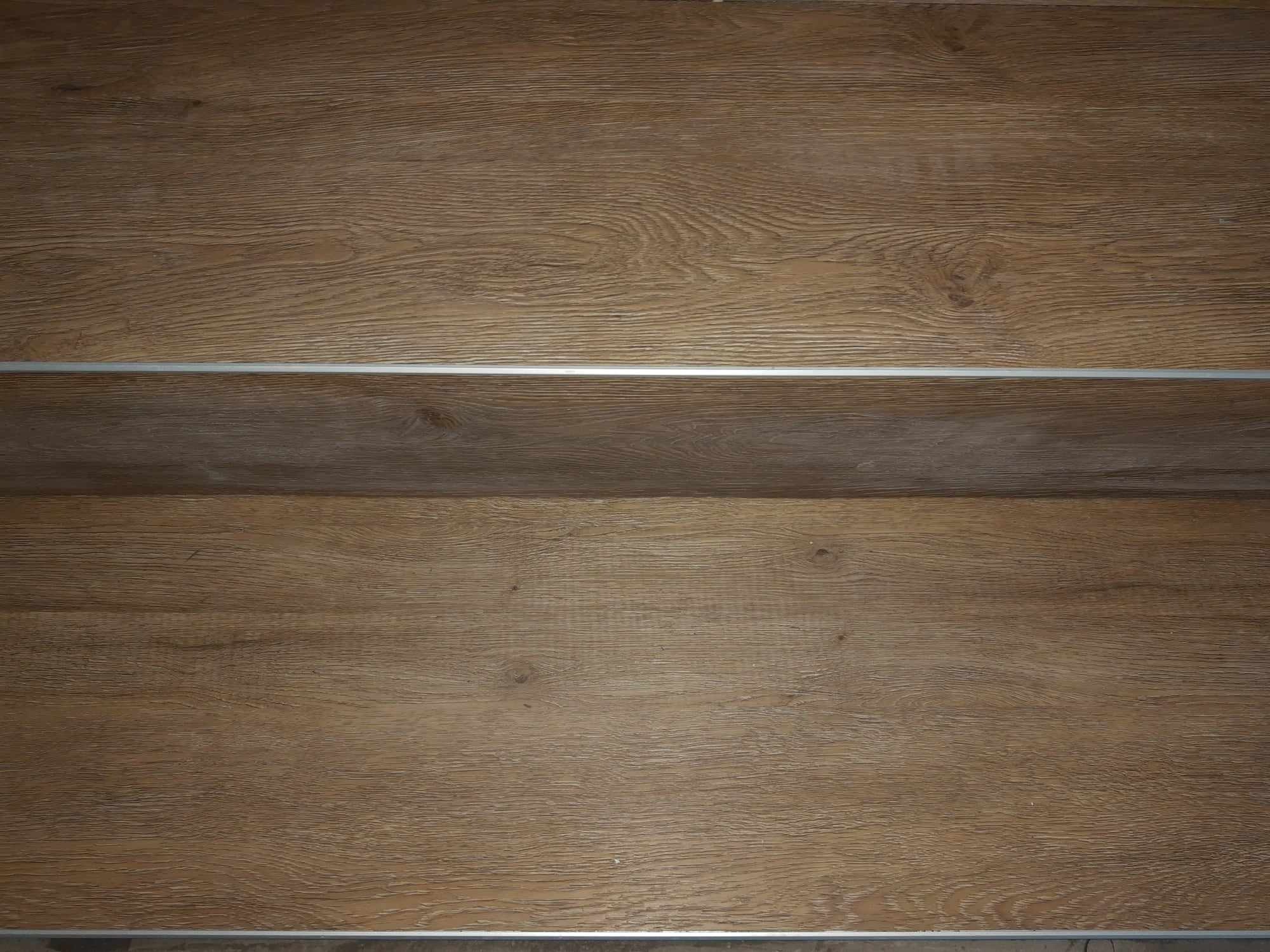 Jasnobrązowe panele podłogowe z wyraźnym rysunkiem drewna, połączone srebrną listwą dylatacyjną.