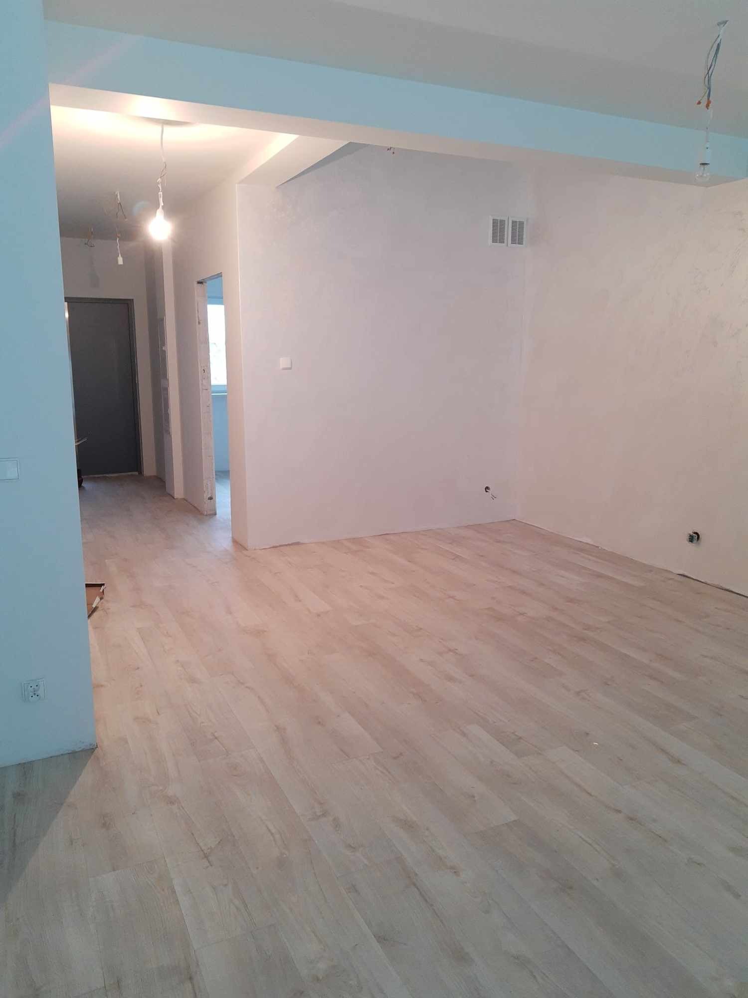 Jasne panele podłogowe ułożone w nowym mieszkaniu w Bydgoszczy, widok na puste, odmalowane ściany i niedokończone oświetlenie sufitowe.