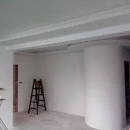 Wnętrze w trakcie remontu: widoczne gładzie na ścianach i suficie, dekoracyjny element sufitu podwieszanego, drabina malarska, przewody na podłodze.