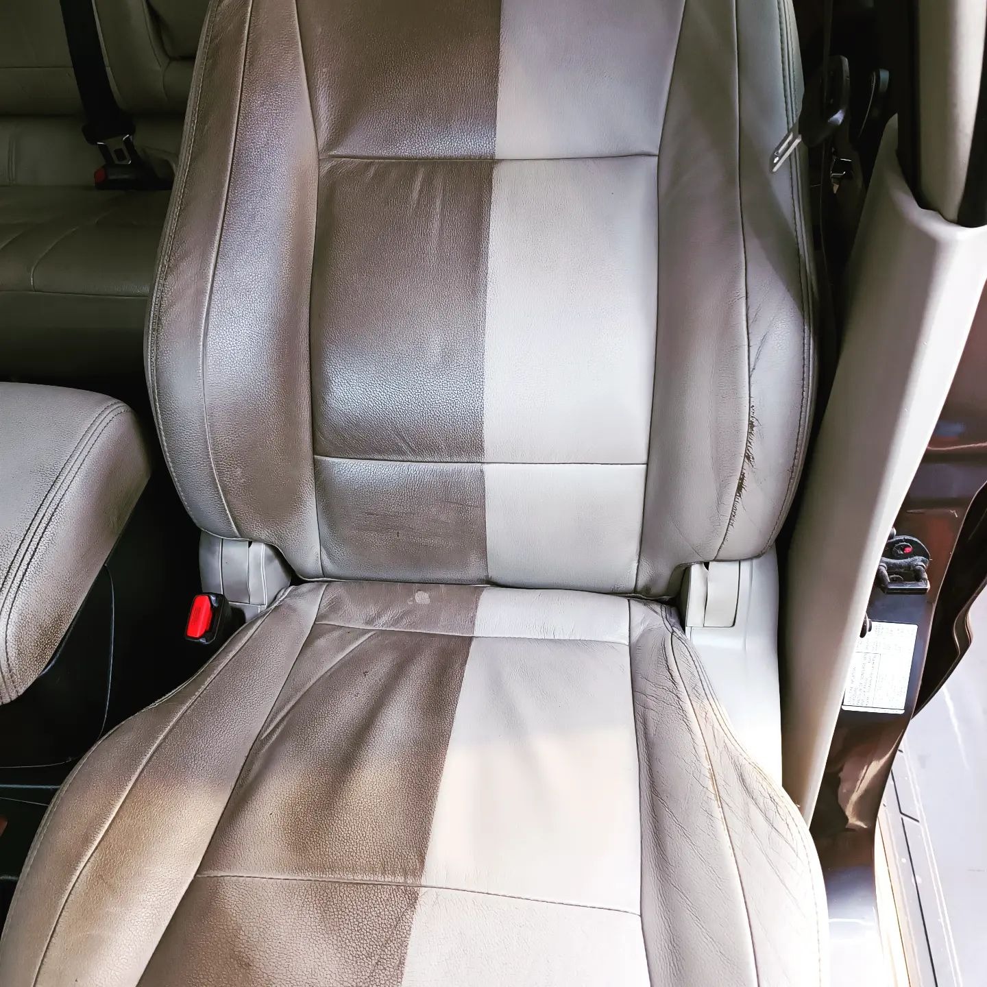 Fotel samochodowy z jasnej skóry, z widoczną różnicą w czystości: połowa wyczyszczona, jaśniejsza, druga połowa brudna, ciemniejsza. Widoczne przetarcia na boku fotela.