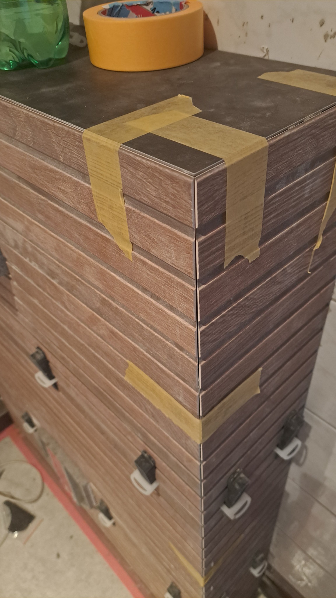 Paczka płytek imitujących drewno, zabezpieczonych taśmą malarską i klipsami poziomującymi, przygotowanych do montażu w Pierzchnicy.