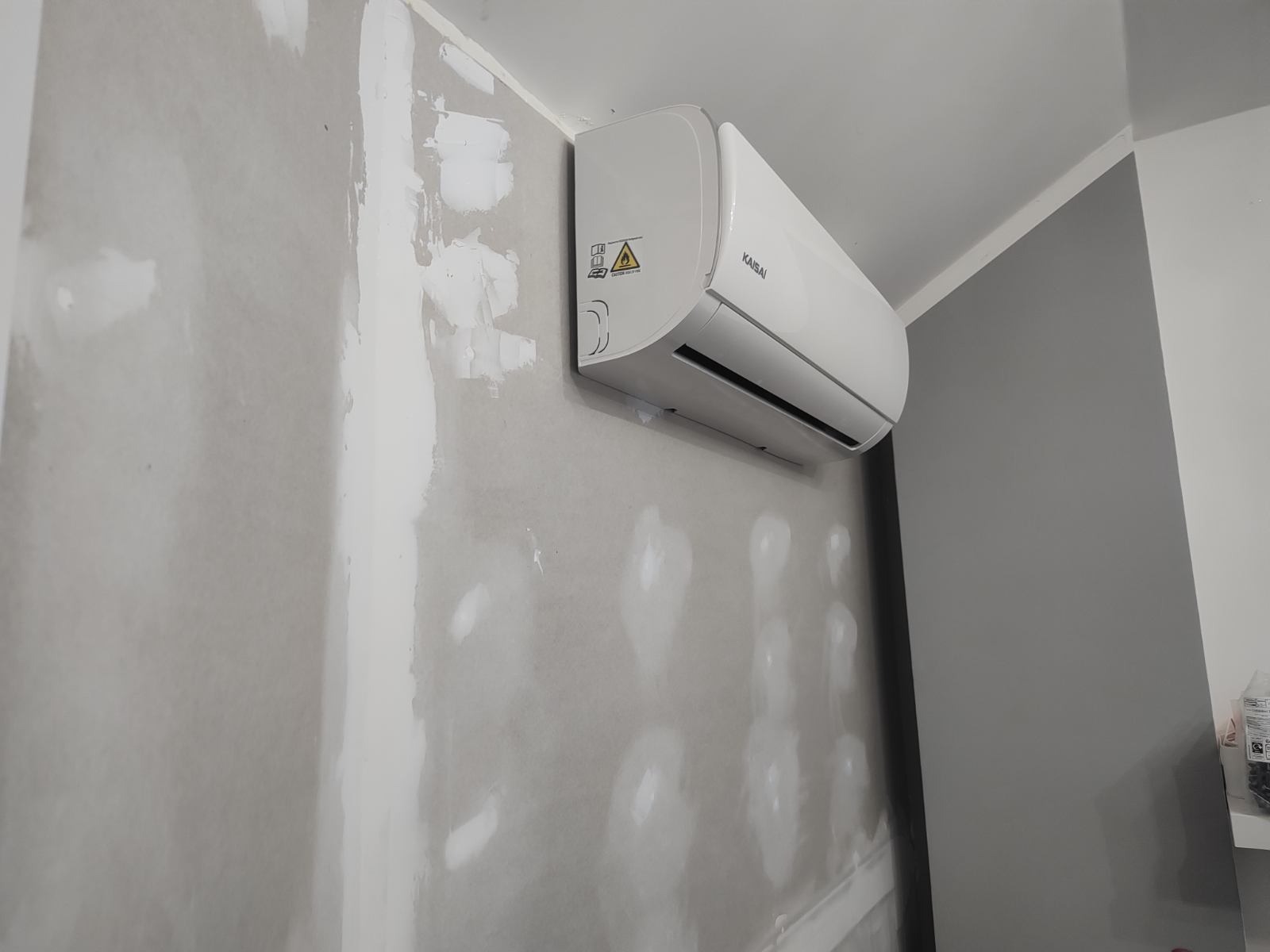 Zamontowany klimatyzator Kaisai na ścianie w trakcie wykańczania, widoczne ślady po szpachlowaniu.