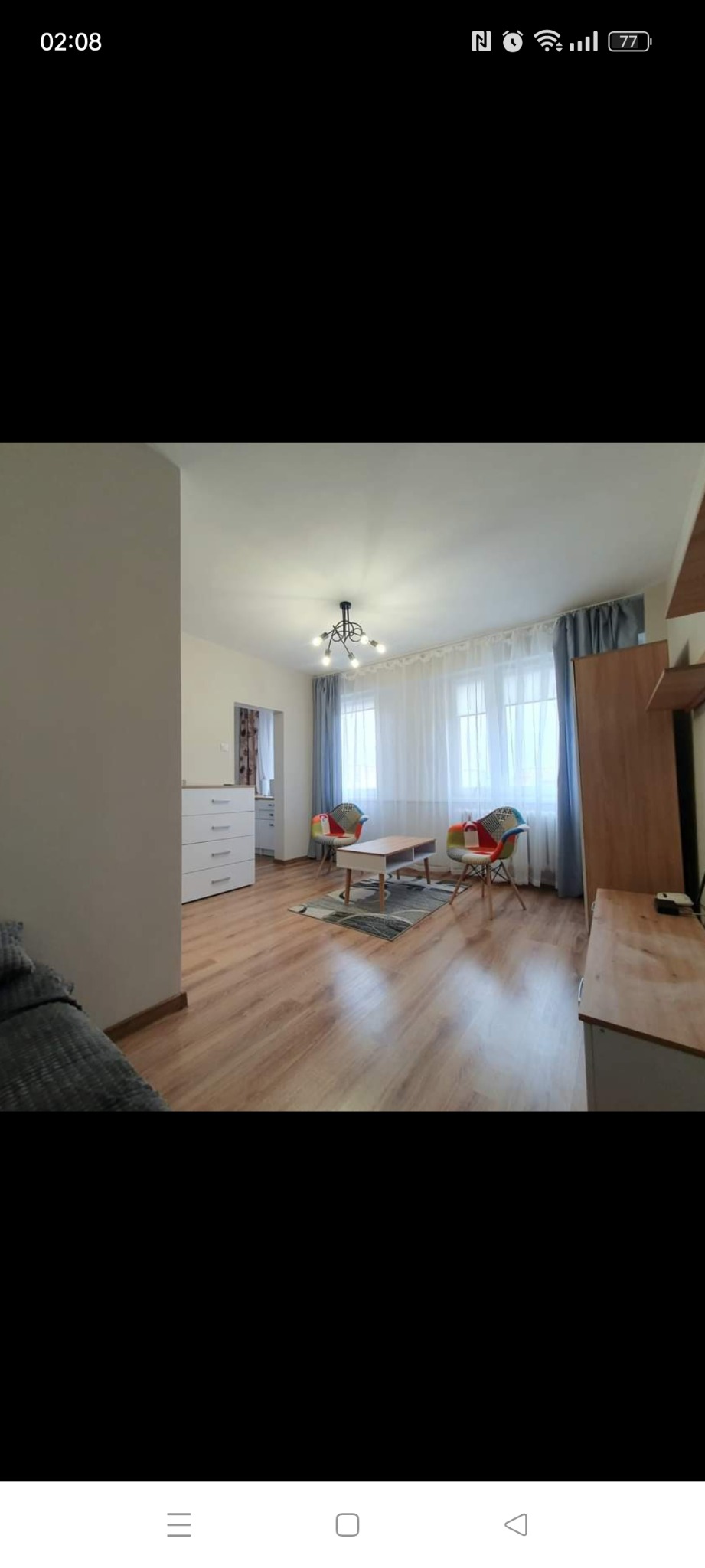 Jasne wnętrze pokoju dziennego z drewnianą podłogą, białymi ścianami, kolorowymi fotelami patchworkowymi i nowoczesnym oświetleniem sufitowym.