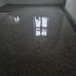 Świeżo wylana, błyszcząca, ciemna posadzka żywiczna z widocznym odbiciem okna, w surowym pomieszczeniu z białymi ścianami.