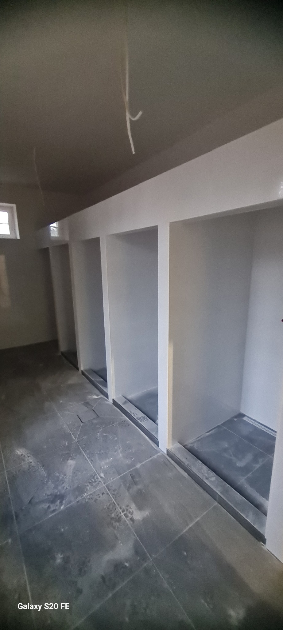 Wnętrze z wnękami wykończonymi na biało i szarą podłogą z płytek. Widoczne niedociągnięcia malarskie i wystające kable. Ujęcie z dołu, perspektywa podkreśla głębię pomieszczenia.