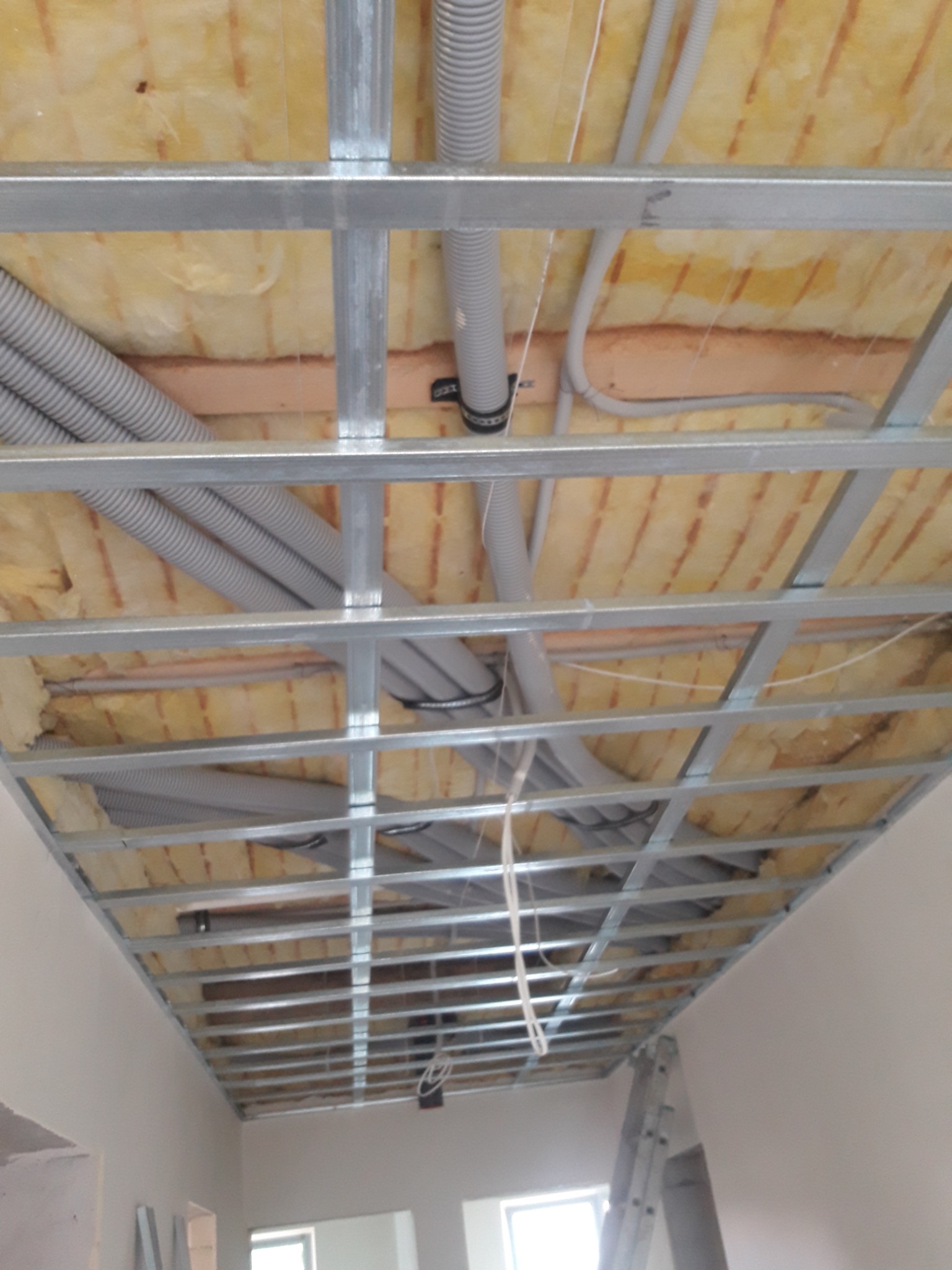 Montaż metalowej konstrukcji sufitu podwieszanego z widoczną izolacją z wełny mineralnej i instalacją elektryczną w rurach karbowanych.