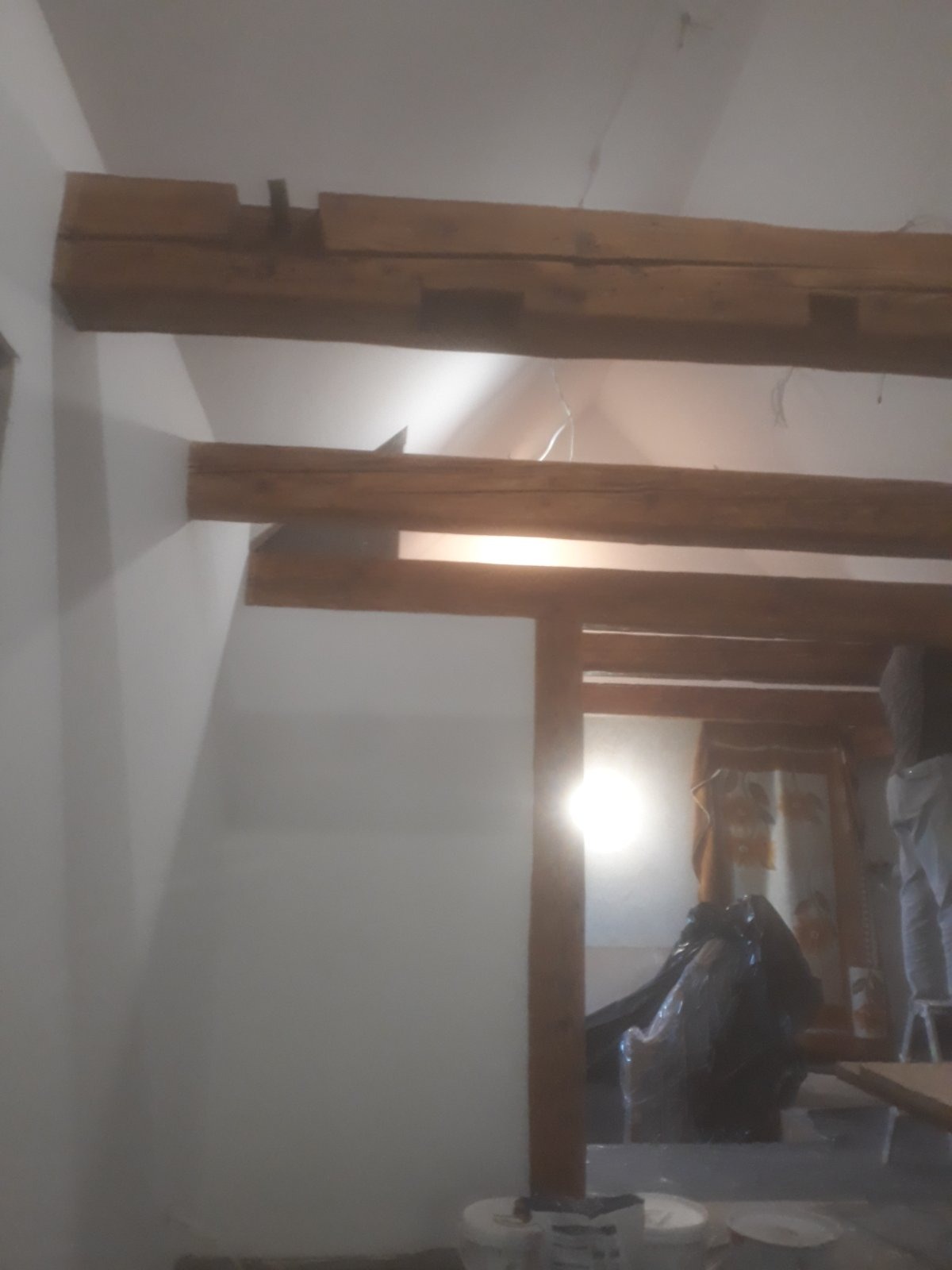 Wnętrze w trakcie remontu z widocznymi drewnianymi belkami stropowymi, częściowo pomalowanymi ścianami i zabezpieczonymi meblami folią ochronną.