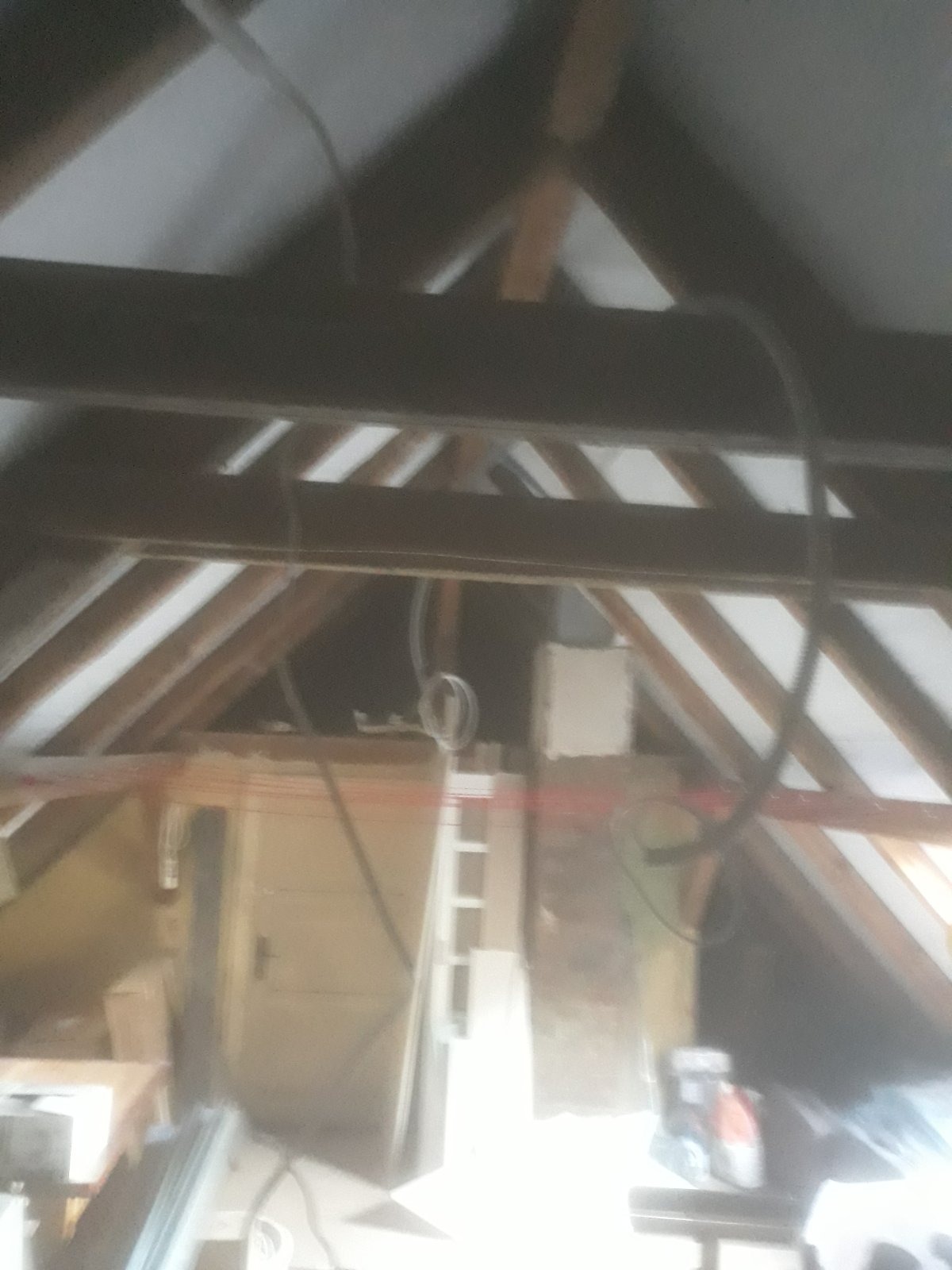 Poddasze w trakcie adaptacji: widoczne drewniane belki konstrukcyjne, izolacja pomiędzy nimi oraz instalacje elektryczne w trakcie montażu. W tle widoczne drzwi i fragmenty ścian.