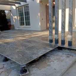 Usługi remontowo - budowlane REM-BUD - Montaż podniesionej podłogi tarasowej z płytek gresowych na regulowanych wspornikach; widoczne słupy konstrukcyjne zabezpieczone folią.