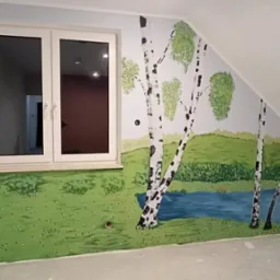 Ręcznie malowana ściana w pokoju dziecięcym przedstawiająca krajobraz z brzozami i jeziorem, widoczna pod oknem oraz na skośnej ścianie poddasza.