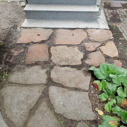 Usługi remontowo - budowlane REM-BUD - Ułożona ścieżka z nieregularnych kamieni prowadząca do granitowych schodów wejściowych, obok rosną kapusty ozdobne.