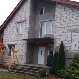 Usługi remontowo - budowlane REM-BUD - Dom w trakcie ocieplania elewacji, widoczne bloki z betonu komórkowego, częściowo zacierane zaprawą, z elementami przygotowanymi pod okna i drzwi, oraz drewniana huśtawka na pierwszym planie.