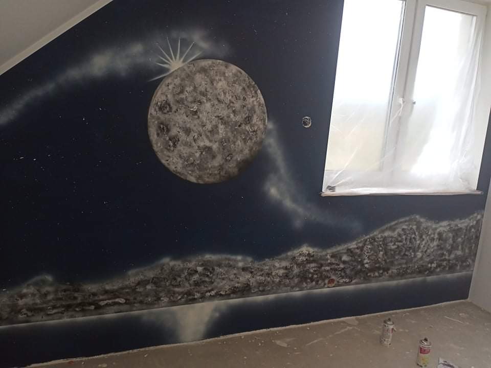 Ściana pokoju po malowaniu artystycznym: motyw kosmiczny z księżycem i gwiazdami wykonany aerografem, okno zabezpieczone folią, puszki farb na podłodze.