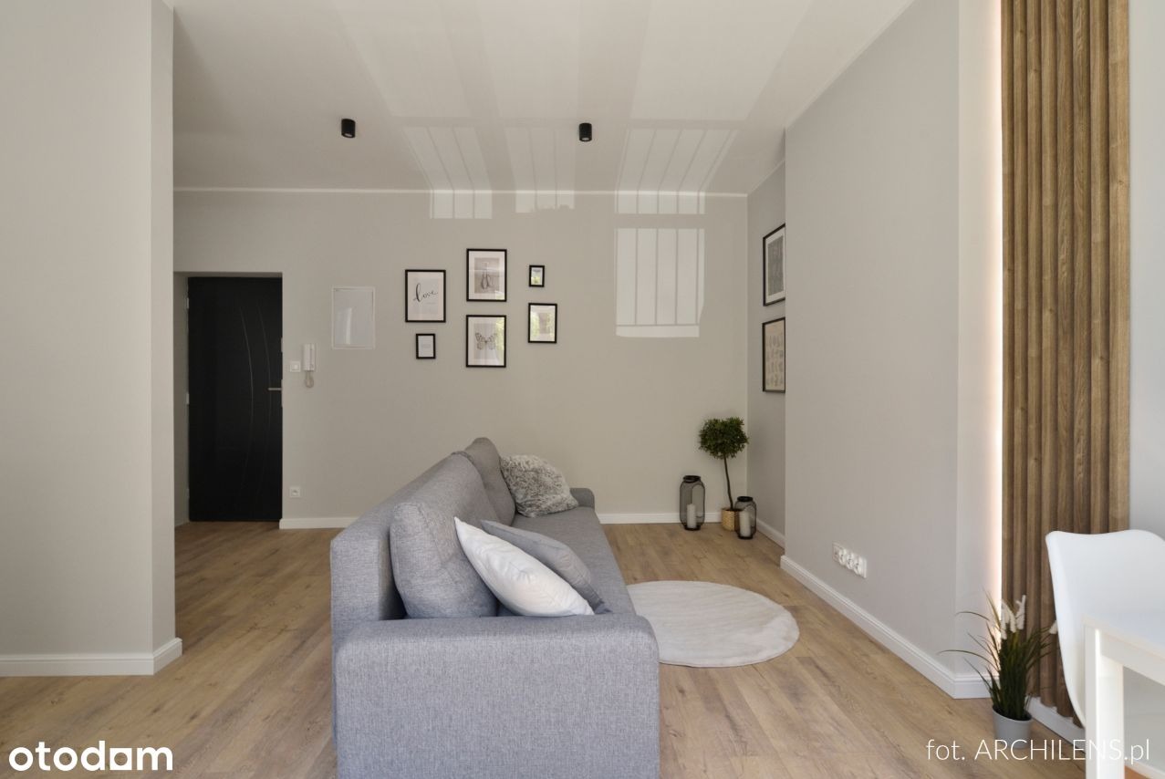 Jasny salon z szarą sofą, drewnianą podłogą i dekoracyjną ścianą z drewnianych paneli z podświetleniem LED.