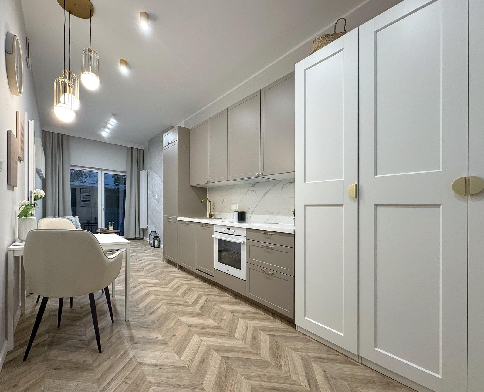 Nowoczesna kuchnia w odcieniach szarości z parkietem ułożonym w jodełkę, złotą armaturą i lampami wiszącymi.