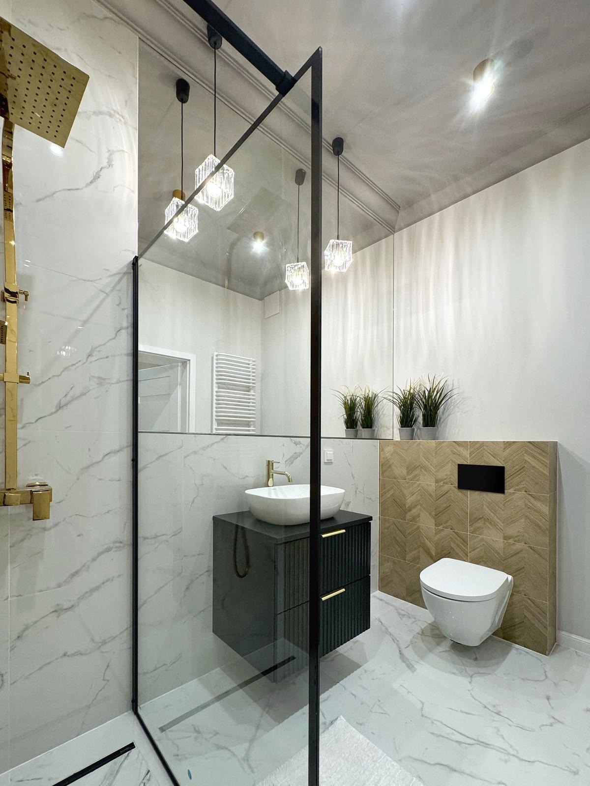 Nowoczesna łazienka z kabiną prysznicową typu walk-in, marmurowymi płytkami, podwieszaną szafką z umywalką nablatową, złotą armaturą i dekoracyjnym oświetleniem.