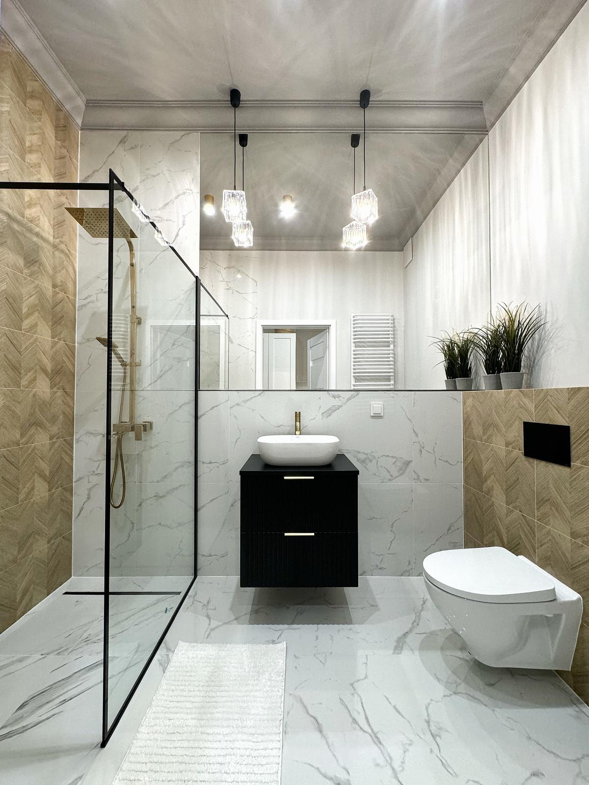 Nowoczesna łazienka z kabiną prysznicową typu walk-in z czarnymi ramami, wiszącą szafką z umywalką nablatową, lustrem na całą szerokość ściany i designerskimi lampami wiszącymi.