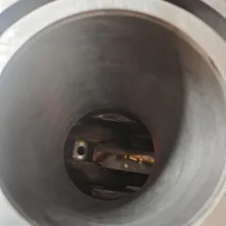 Wnętrze cylindra silnika spalinowego, widoczny tłok i korbowód w słabym oświetleniu warsztatowym.